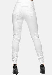 Jeans blancos ajustados con una textura suave, que cuentan con bolsillos traseros y un corte entallado. Llevados con zapatos de tacón negro.