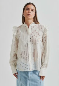 Lightweight white blouse featuring textured fabric with cut-out patterns, ruffled shoulders, and a button-down front.