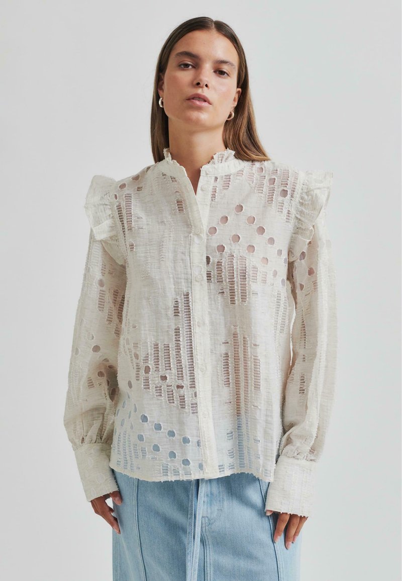 Lightweight white blouse featuring textured fabric with cut-out patterns, ruffled shoulders, and a button-down front.