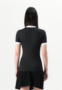 Svart kortermet skjorte med hvit krage og akkompagnement på ermene, med en tettsittende design og glatt tekstur. Brukt med et svart utsvingt skjørt.