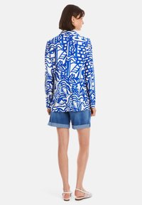 Langärmliges Hemd mit einem blau-weißen abstrakten Muster, aus leichtem Stoff; kombiniert mit hochgerollten Jeansshorts und Riemchensandalen.