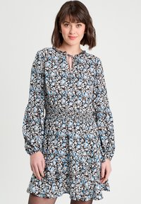 Robe florale avec un fond noir, ornée de fleurs bleues et blanches, décolleté en forme de clé, et longues manches bouffantes avec un ourlet froncé.