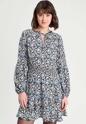 Robe florale avec un fond noir, ornée de fleurs bleues et blanches, décolleté en forme de clé, et longues manches bouffantes avec un ourlet froncé.