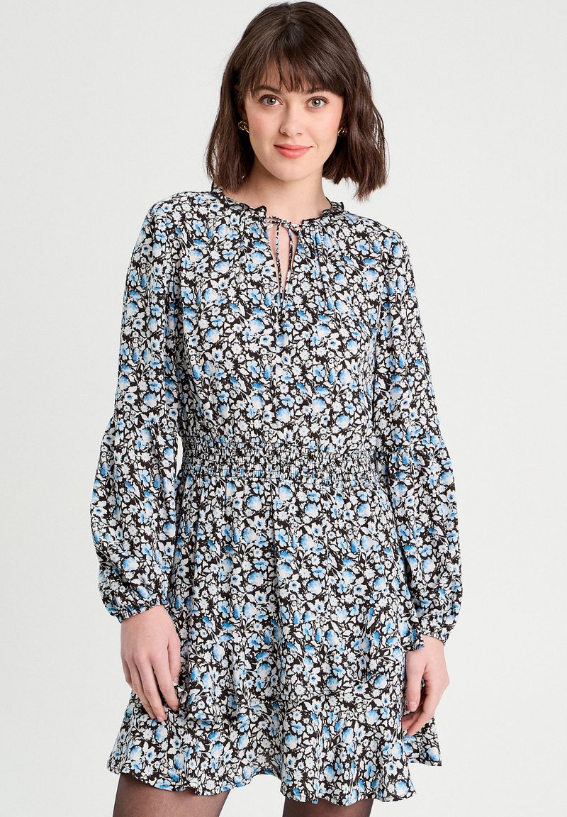 Robe florale avec un fond noir, ornée de fleurs bleues et blanches, décolleté en forme de clé, et longues manches bouffantes avec un ourlet froncé.