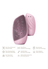 Appareil de nettoyage facial en silicone de couleur rose pâle, avec une surface texturée dotée de nodules surélevés, une forme ergonomique et des boutons de commande intégrés.