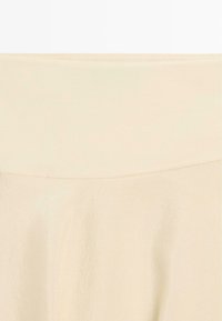 Beige stof met een brede tailleband, een gladde textuur en lichte kreukels onder de tailleband.