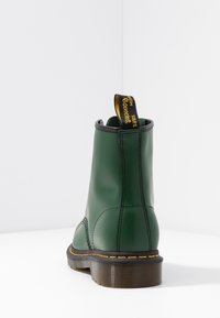 Green leather ankle boot with black accents, rubber sole, and yellow pull tab. Stitching detail along the sides, sturdy design.
