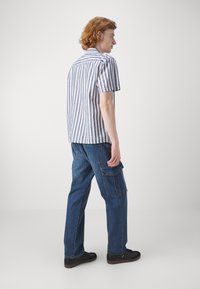 Stripet skjorte med korte ermer i blått og hvitt, kombinert med mørk denim cargo-bukser med lommer. Sorte sneakers fullfører antrekket.