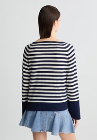 Maglione a righe navy e bianche con una vestibilità rilassata, scollatura ampia e maniche lunghe; abbinato a una gonna denim svasata.