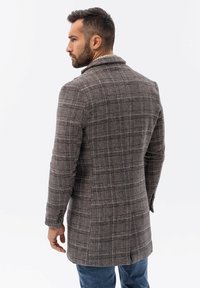 Ruskea ruudullinen päällystakki, jossa on muotoiltu malli, napitettu kaulus ja nappidetaileja. Sisältää tekstuurista materiaalia ja kaksinkertaisen halkion takana.