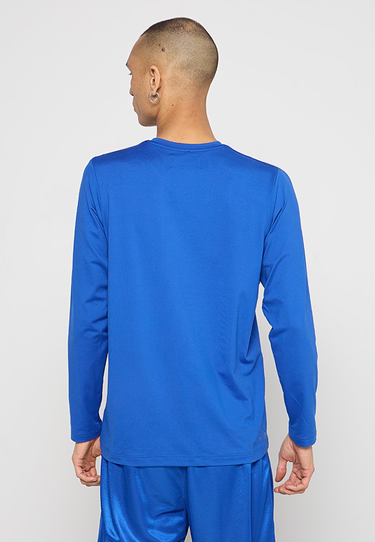T-shirt de sport à manches longues en tissu bleu vif, avec un col rond et une texture lisse. Porté avec un short bleu assorti.