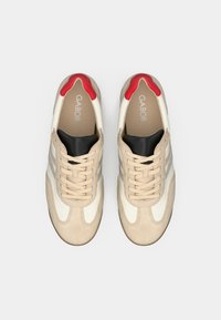 Ζευγάρι μπεζ και λευκά αθλητικά παπούτσια Gabor με κόκκινες λεπτομέρειες στις φτέρνες, μαύρους γλωσσικούς και μπεζ κορδόνια, απεικονιζόμενα από πάνω σε λευκό φόντο.