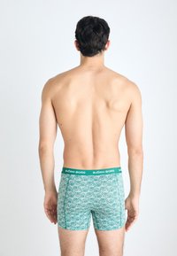 Grønne mønstrede boxershorts med en sort linning, der har "BJÖRN BORG"-logoet. Stofkvaliteten er glat med geometriske designelementer.