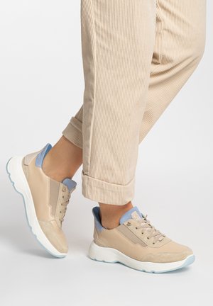 Person wearing beige and light blue sneakers with beige corduroy pants, showing side and back view of shoes on white background.