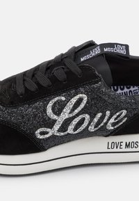 Baskets noires avec un panneau pailleté affichant "Love" en argent, lacets noirs et logo "Love Moschino" sur la languette et la semelle.