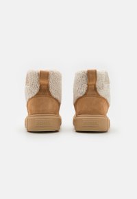 Visoke čizme s donjim dijelom od smeđeg suede materijala i gornjim dijelom od kremastog umjetnog ovčjeg krzna, s teksturiranim gumenim đonom i logotipom straga.