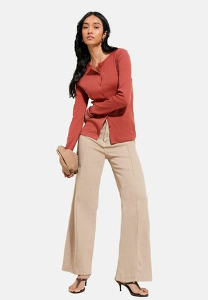 Langärmliges Hemd in Rostfarbe mit Knöpfen, kombiniert mit beigen, weit geschnittenen Hosen. Das Outfit besticht durch ein strukturiertes Material und ein schlichtes Design.