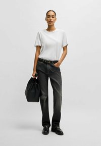 Maglietta bianca a maniche corte, jeans scuri a vita alta, cintura nera e borsa tote in pelle nera, con mocassini neri. Design semplice.