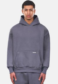 Grauer Kapuzenpullover aus weichem Material. Verfügt über eine Kängurutasche sowie gerippte Bündchen und Saum. Schlichtes Design mit einem kleinen Markenetikett.
