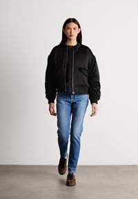 Jachetă neagră bomber cu manșete ribbate și buzunare frontale, asortată cu blugi albaștri și pantofi sport cu imprimeu animal. Material neted, design scurt.