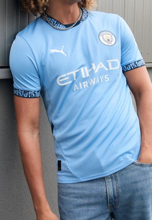 Maillot de football bleu clair à manches courtes, avec des accents noirs en motif sur le col et les poignets, logo Puma et texte ETIHAD AIRWAYS.