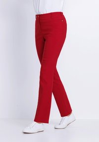 Rote Hosen mit schmaler Passform, aus einem glatten Baumwollgemisch, im klassischen Design, mit Seitentaschen und kombiniert mit weißen Turnschuhen.