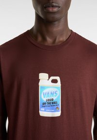 Kastanjaberg-särkilä T-paita, jossa on grafiikka nestesäiliöstä ja teksti "VANS LIQUID OFF THE WALL" sinisellä ja valkoisella.