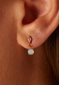 Goudkleurige oorbellen met een druppelontwerp, voorzien van een marquise-vormige roze edelsteen en een ronde lichtblauwe steen, gezet in metalen accenten.