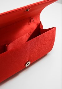 Rode stoffen clutch met een gladde textuur, een drukknoopsluiting en binnenvakken voor organisatie. Geen zichtbare merknaam of patronen.