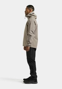 Chaqueta impermeable gris claro con capucha, mangas largas y puños elásticos, combinada con pantalones ajustados negros y botas negras resistentes.