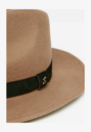 Beige Filzhut mit breiter Krempe, ausgestattet mit einem dunkelbraunen Lederband und einem dekorativen Messingakzent an der Seite. Weiche Textur durchgehend.