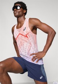 Sportieve tanktop met een gemêleerd patroon in rood en wit, gecombineerd met een marineblauwe short. Geaccessoireerd met strakke zwarte zonnebril.