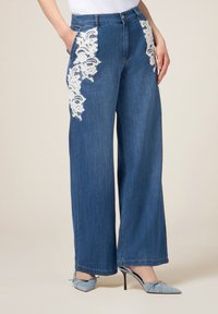 Jeans de mezclilla de pierna ancha en azul medio con bordado de flores de encaje blanco en los bolsillos delanteros. Presenta una cintura alta y diseño clásico de cinco bolsillos.