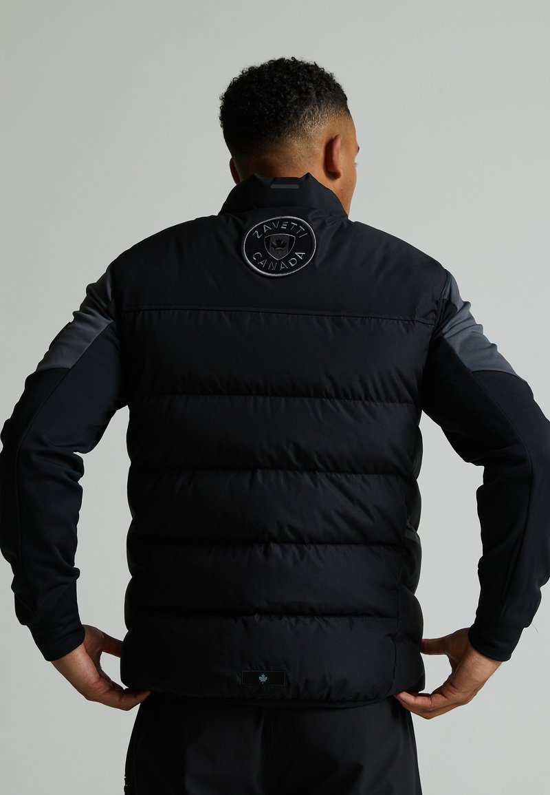 Doudoune noire avec une finition mate, présentant un logo rond au dos, des accents gris aux épaules et un design élégant et ajusté.
