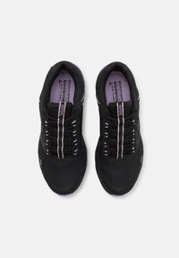 Chaussures de sport noires avec un tissu en maille, accents violets, lacets plats et semelle texturée. Présente un design minimaliste et un talon sécurisé.