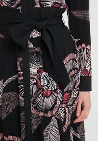 Czarna sukienka w kwiatowy wzór w odcieniach różu i bieli. Posiada przewiązywany pas w talii oraz długie rękawy. Wykonana z miękkiego, delikatnego materiału z teksturowanym motywem liści.
