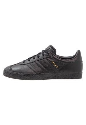 Czarny skórzany sneaker Adidas Gazelle z czarnymi sznurowadłami, fakturowaną podeszwą i złotym napisem "GAZELLE" z boku.