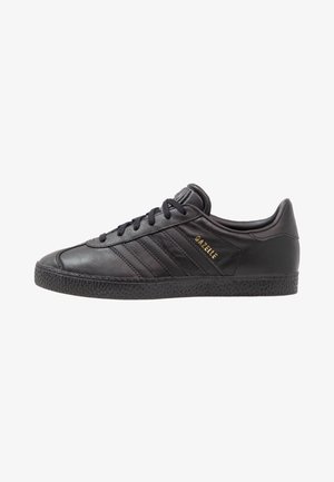 Schwarzer Adidas Gazelle Ledersneaker mit schwarzen Schnürsenkeln, strukturierter Sohle und goldener "GAZELLE"-Beschriftung an der Seite.