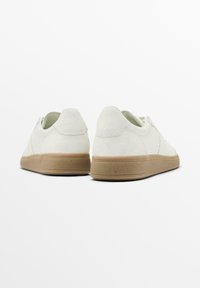 Sneaker bianchi in suede con un design a collo basso, dotati di una suola in gomma beige testurizzata e dettagli di cucitura minimali.