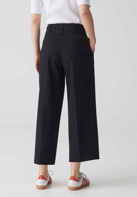 Zwarte wijde broek met een hoge tailleband, twee achterzakken, gecombineerd met witte sneakers met rode accenten en een gumrubberen zool.