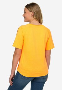 Felle oranje T-shirt met korte mouwen en een ronde halslijn, met een ontspannen pasvorm. De stof lijkt zacht en tekstuurrijk, ontworpen voor casually gebruik.