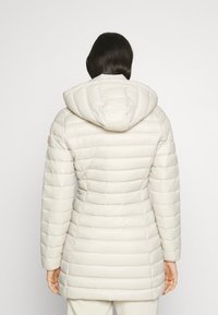 Letvægts polstret vinterjakke i creme med quiltet design, justerbar hætte og slim fit. Har diskret orange branding på ærmet.