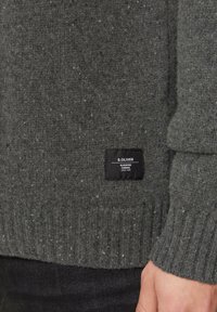 Ciemnoszary sweter z przędzy ze ściągaczami przy mankietach i u dołu. Posiada czarną metkę z białym napisem, wskazującą na markę S. OLIVER.