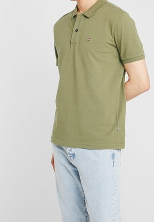 Polo de color verde olivo hecho de algodón. Cuenta con un collar abotonado y un pequeño logo en el pecho. Combinado con jeans de color azul claro.