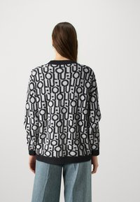 Maglione lavorato a maglia con un motivo geometrico in nero e grigio, caratterizzato da un collo rotondo, maniche lunghe e polsini a coste. Design loose-fit.