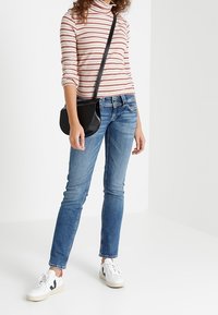 Modré denimové džíny slim fit, s vybledlým odstínem a jemným praním. V kombinaci s proužkovaným rolákem a bílými teniskami. Černá crossbody taška.