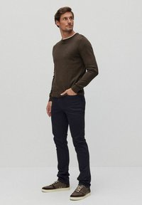 Brun tröja i stickat material, kombinerad med mörka byxor och bruna sneakers. Noterbara detaljer inkluderar en rundad halsringning och en strukturerad tyg.