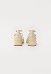 Beiga lackläderskor med klack och en rem bak med spänne, med en slät yta och rundade kanter.