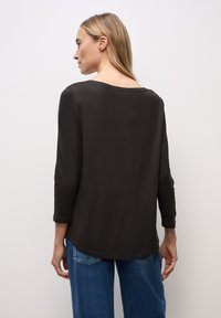 Schwarzes Langarmoberteil mit weitem Ausschnitt, weichem Material und abgerundetem Saum, kombiniert mit blauen Jeans.