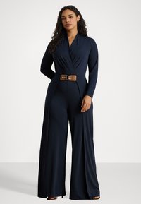 Tuta navy con maniche lunghe, design avvolgente, cintura larga con fibbia marrone e pantaloni a gamba larga con una texture liscia.